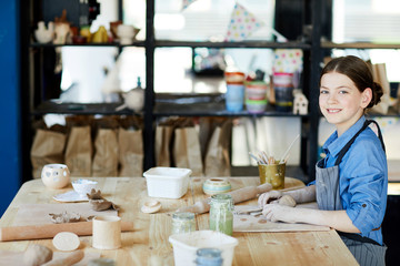 Happy creative schoolgirl looking at camera while sitting by table at lesson of creative crafts