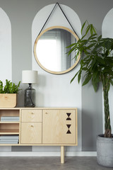 Round mirror above wooden cabinet with lamp in minimal flat interior with plants. Real photo