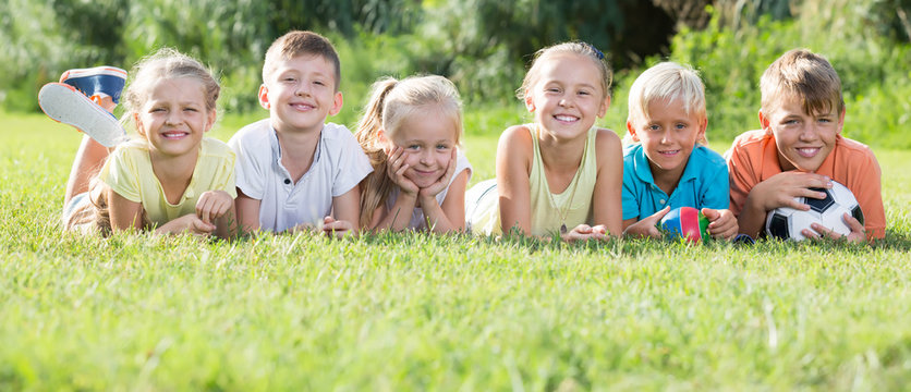 Group Of Friendly Kids Lying On Green Grass In Park
