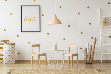Pastel lamp above table and wooden chairs in gold child's room interior with poster. Real photo