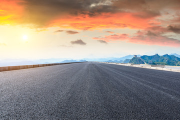 Empty asphalt road and great wall with mountains at sunset