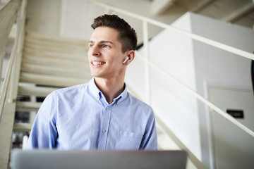 Fototapeta premium Young contemporary businessman in earphones sitting on staircase and enjoying music during work