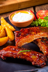 bbq spareribs on the plate with green salad and white sauce.