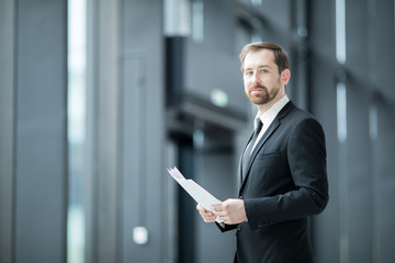 Young bearded businessman in suit standing in front of camera and looking at you