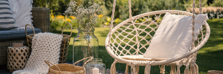 Pillow on hanging chair on terrace with blanket in basket next to flowers. Real photo