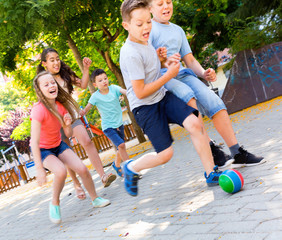Happy children  playfully running after ball outdoors in park