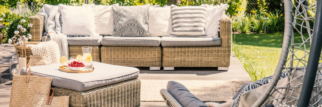 Panorama of rattan sofa with pillows and table on terrace in the garden. Real photo