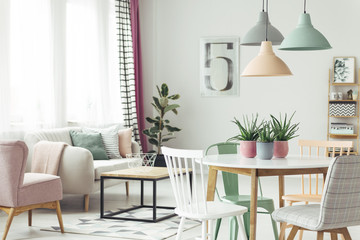 Real photo of a pastel living room interior with a dining table, chairs, lamps, coffee table and sofa