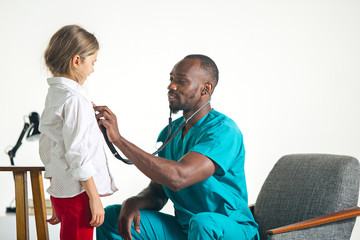 Fototapeta premium The healthcare and medical concept - african male doctor with stethoscope listening to child chest in hospital. The doctor, health, medicine, patient, pediatrician, illness concepts