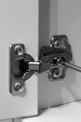 Screwing hinge on a white cupboard to adjust the door with a screwdriver