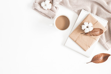 Autumn or winter composition. Cup of coffee, gift, dried autumn leaves, beige sweater on white background. Flat lay, top view, copy space