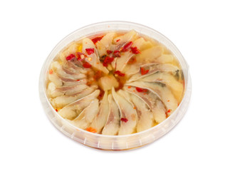 Slices of pickled herring in container with red pepper marinade