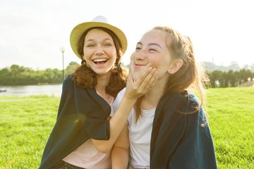 Young girls having fun sitting on green grass lawn. Background nature, recreation area, river.