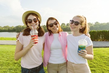 Portrait of happy mother and daughters teenagers 14 and 16 years old, girls with summer drinks. Background nature, recreation area, river.