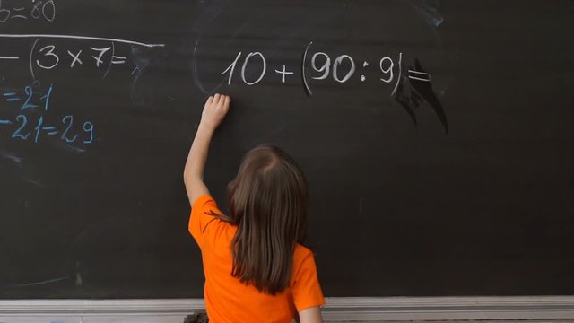 A little girl draws chalk on a blackboard.