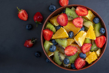 Bowl of healthy fresh fruit salad on dark background. Top view.
