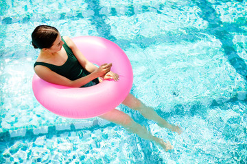 Restful girl inside pink pool buoy balancing on water and enjoying sunny day at spa resort