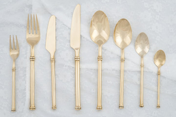 Set of eight pieces of bronze flatware, spoons forks and knife, on white cloth backgroud