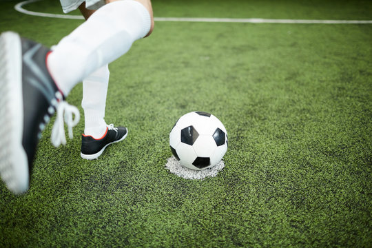 Leg of footballer before kicking soccer ball during game of football on green field