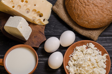 Rural breakfast. Bread, cheese, feta, cottage cheese, milk and eggs on a wooden black table. Top view.