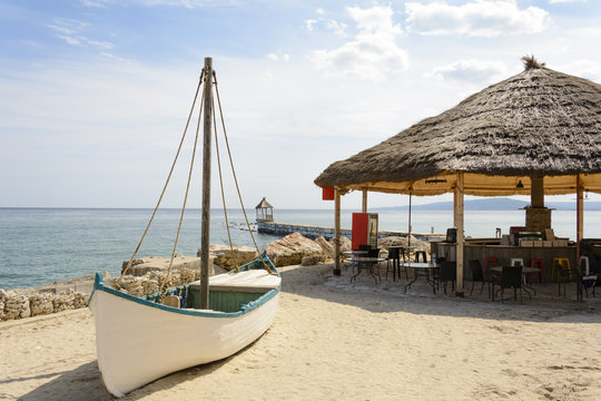Bar on a beach with a sailing boat and a pier.