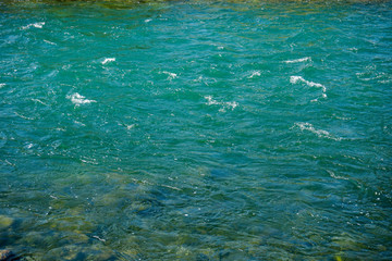 Fototapeta na wymiar turquoise river water with small waves and stones