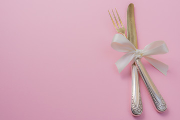 Silver fork and knife with white ribbon on pink background