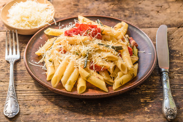 Classic Italian pasta with zucchini and tomatoes in a clay tartle on old wooden rustic table