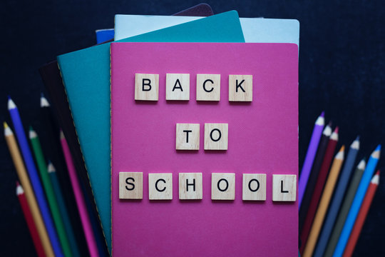 Close-up Pile Of Books, School Stationery, Wooden Words Back To School On Slate Black Background. Back To School Concept. Top View.