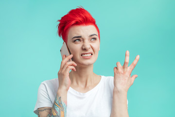 emotional frustrated angry girl with short pink hair is talking on the phone. young woman is angry...