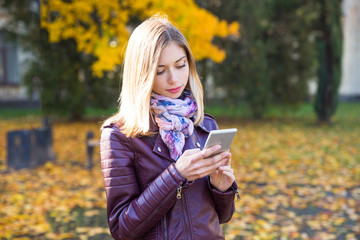 Happy teen girl with phone smile during walking on autumn park. Fall concept