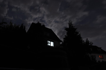 einzelnes erleuchtetes Fenster bei Nacht in einem von Bäumen umgebenen Haus