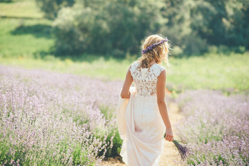 Fototapeta na wymiar Beautiful young woman bride is walking on the lavender field