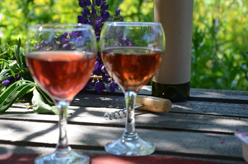 Red wine poured into wine glass on background of green tree leaf foliage. purple flower