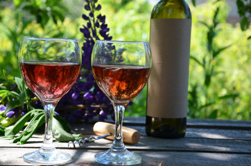 Red wine poured into wine glass on background of green tree leaf foliage. purple flower