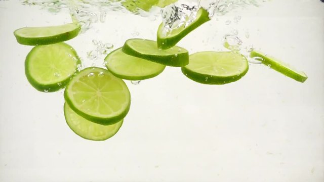 Round lime slices slowly sink in water, slow motion close-up