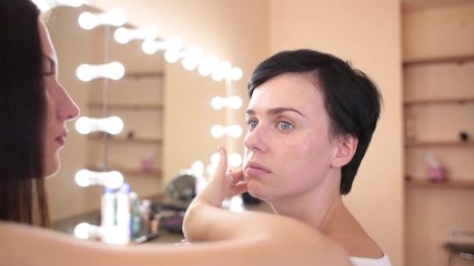The make-up artist applies a cream on the face of the girl before visage.