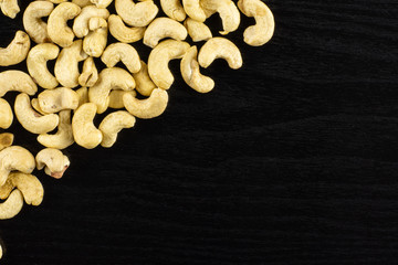 Lot of whole raw cashew nut upper corner flatlay on black wood