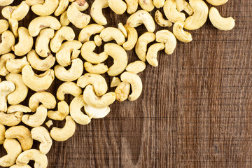 Lot of whole raw cashew nut upper corner flatlay on brown wood
