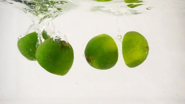 Juicy halves of lyme fall into the water with bubbles and spray, then the lemon falls, slow motion close-up