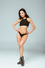 Obraz premium Sexy woman in sport bra and panties posing with hands akimbo, on grey