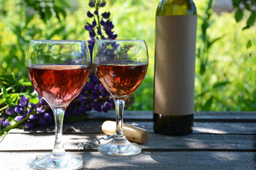 Red wine poured into wine glass on background of green tree leaf foliage. purple flower