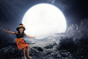 Happy asian child girl in witch costume and hat sitting