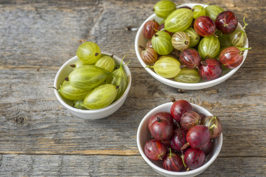 Gooseberry berries are red and white in a plate on a wooden rustic background.