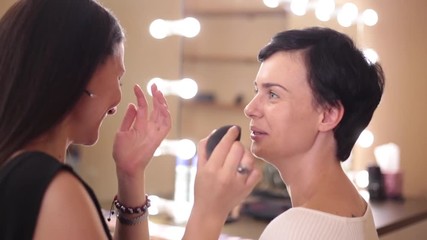 The make-up artist communicates cheerfully with the girl applying a foundation cream