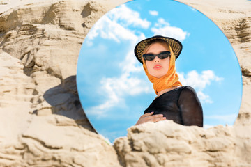 round mirror with reflection of beautiful stylish model in hat and sunglasses