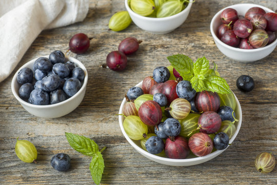 Summer gooseberry and blueberry berries in a plate on a wooden rustic background.