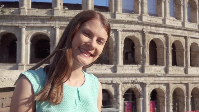 Young woman standing on background of famous Roman attraction Colosseum in Rome, Italy in slow motion. Happy female tourist enjoying her european summer vacation. Student travel through Europe