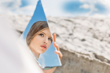 charming girl holding piece of mirror and looking on her reflection