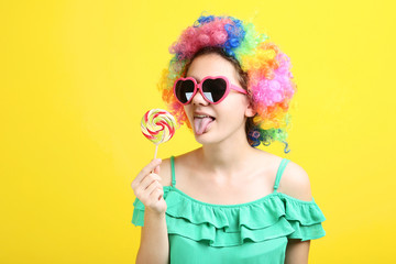 Young girl in clown wig and lillopop on yellow background